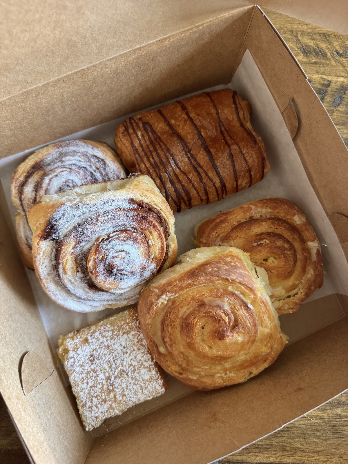 A kraft box of cinnamon swirls, kouign-amann and a lemon bar